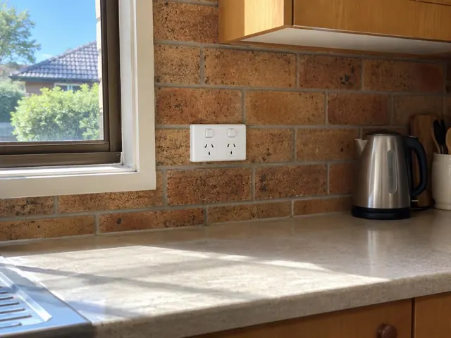 Double power point on a brick kitchen splashback beside a window and benchtop in Kellyville
