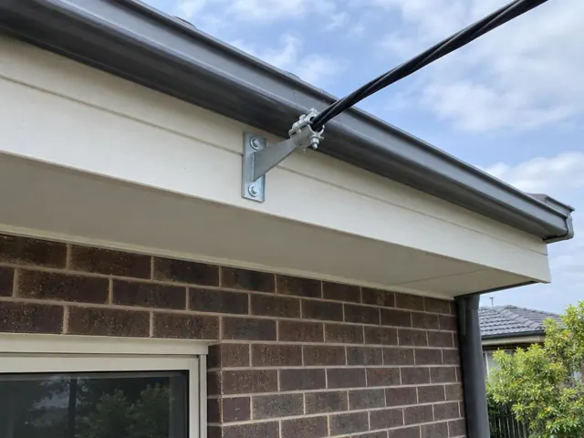 Overhead service cable and bracket mounted on a house fascia above brick wall in Beaumont Hills